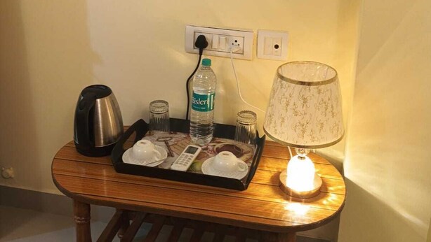 Una pequeña mesa de madera con una bandeja que contiene una tetera, una botella de agua, vasos y una lámpara de mesa pequeña.