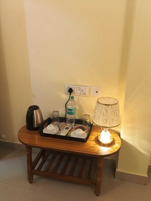 A small wooden table with a tray containing a kettle, a bottle of water, glasses, and a small table lamp.