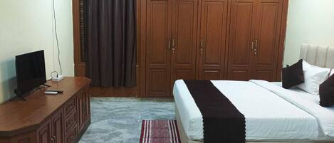 A bedroom with a bed, a TV on a wooden cabinet, and a wardrobe.