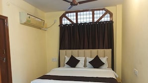 Un dormitorio con cama, ventilador de techo, aire acondicionado y ventana con cortinas.
