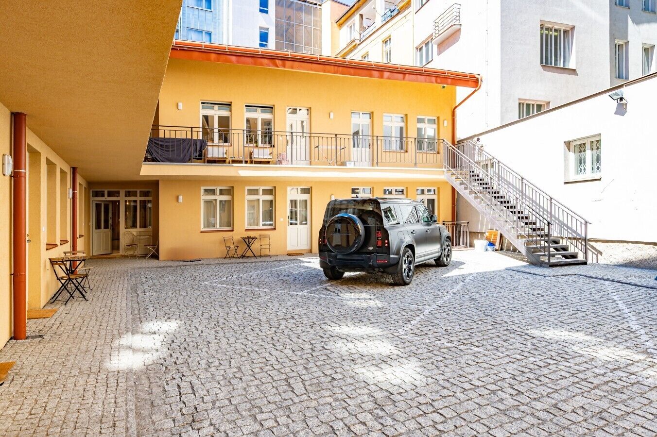 Une cour intérieure avec un VUS garé, un escalier et un bâtiment doté de nombreuses fenêtres et de balcons.
