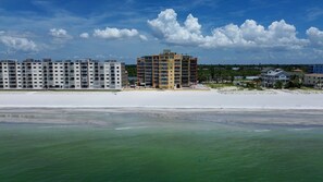 Ein Strandhotel mit mehreren Etagen, einem Sandstrand davor und einem klaren Himmel.