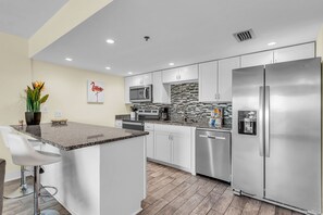 A modern kitchen with stainless steel appliances, a granite countertop, and a central island with bar stools.