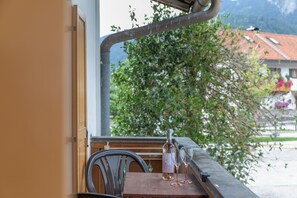 A table with a bottle and two glasses, a chair, and a view of a tree and buildings.