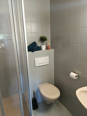 Un baño con inodoro, lavabo, ducha y perchero para toallas.