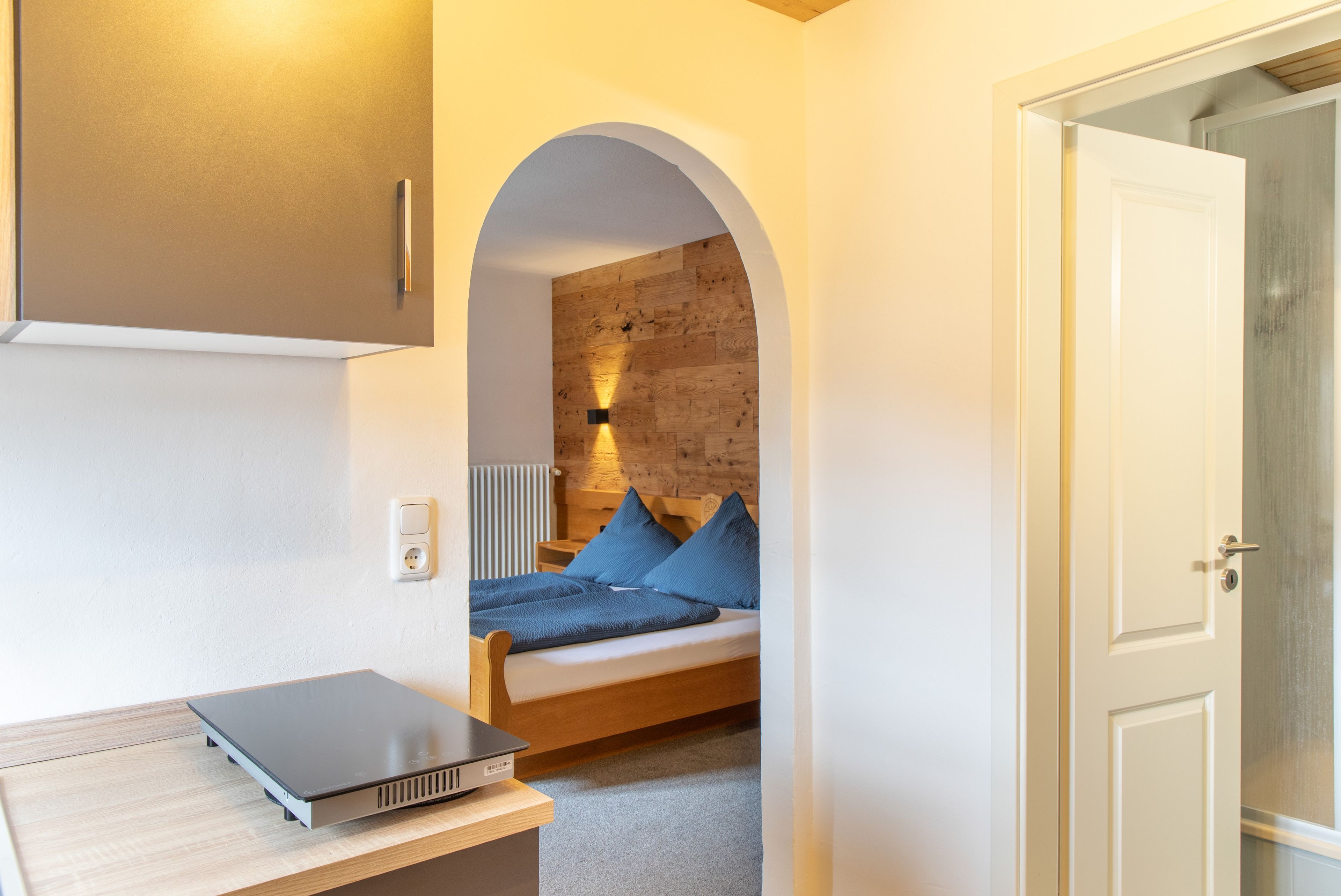 A bedroom with a bed, a desk with a laptop, a door, and a wall with a wooden panel.