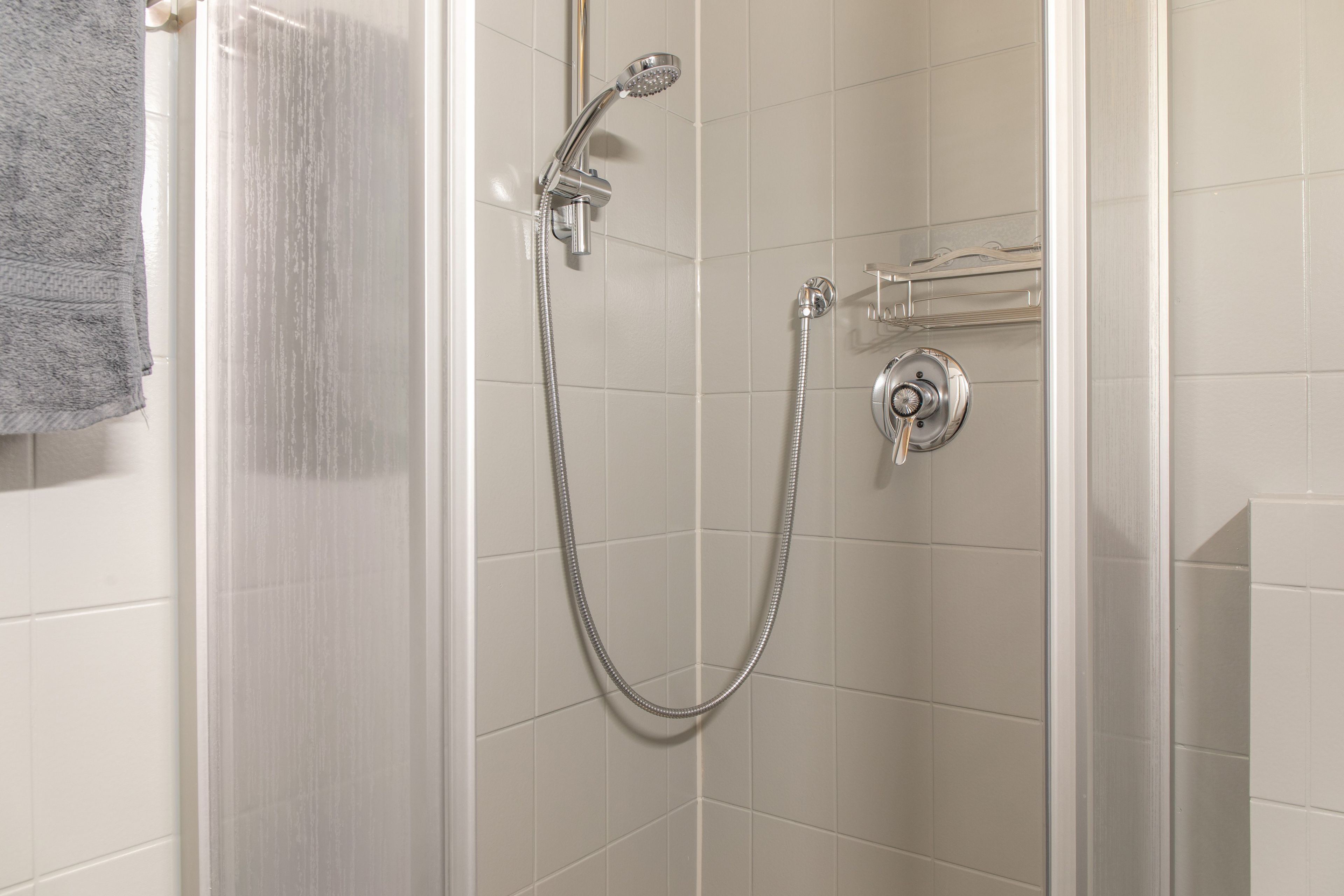Une douche équipée d’un pommeau de douche à main et d’un robinet fixé au mur.