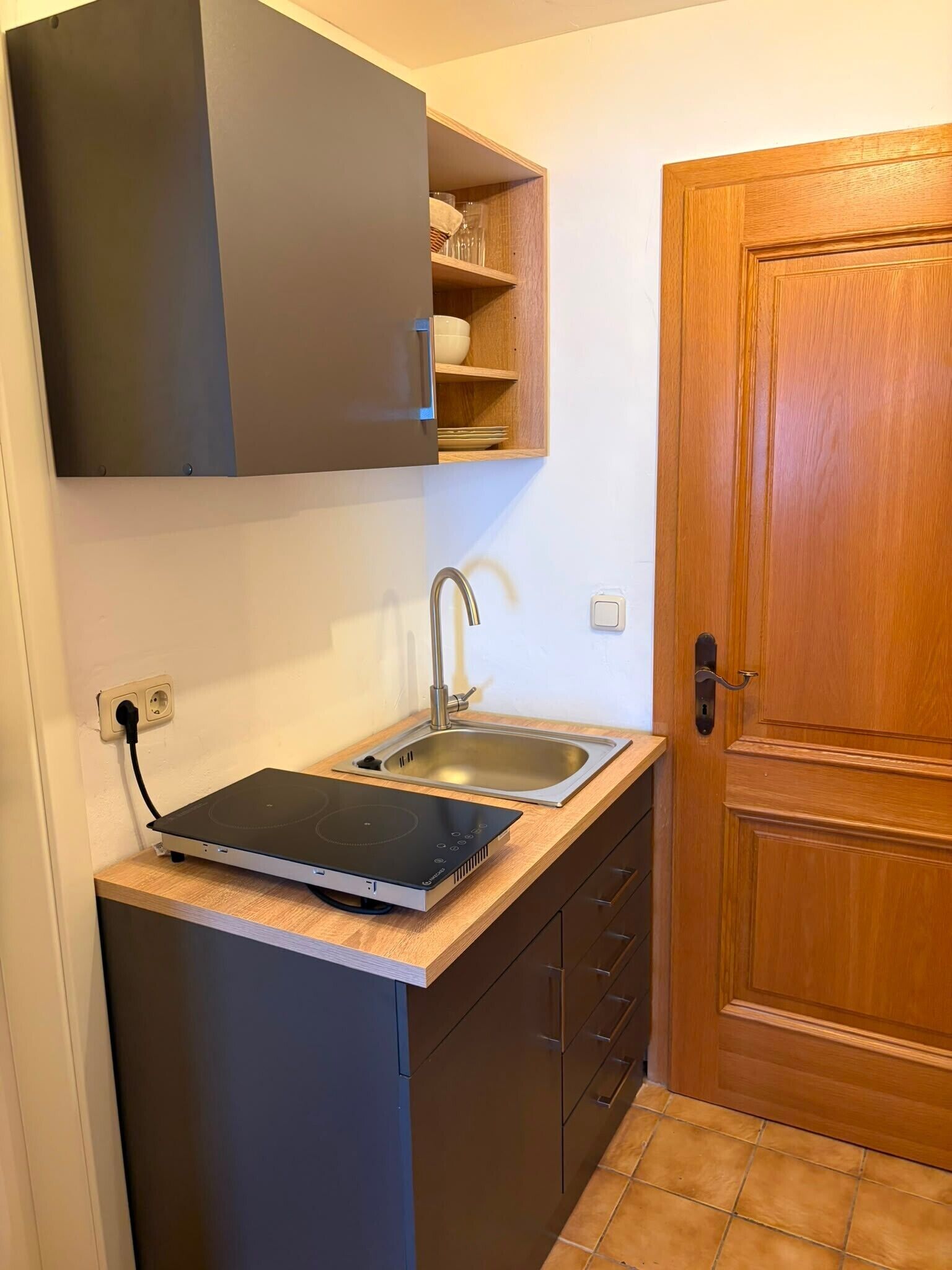 Una cocina compacta con lavavajillas integrado, un lavabo y una puerta de madera.