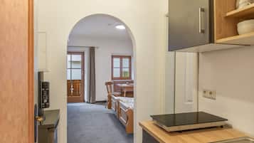 Um corredor estreito leva a uma área de refeições com mesa e cadeiras de madeira, uma cozinha com forno embutido e uma porta com painel de controle.