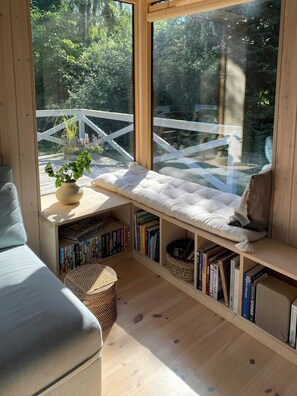 A cozy reading nook with a cushioned bench, a bookshelf, and a window overlooking a wooden deck. - Holiday home with enchanting garden in Kulhuse (Jægerspris)