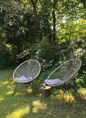 Two wicker chairs with cushions, placed on grass in a garden with dense foliage and trees in the background. - Holiday home with enchanting garden in Kulhuse (Jægerspris)