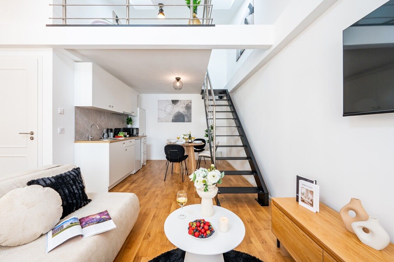 A modern apartment with a kitchen, dining area, and a staircase leading to an upper level.