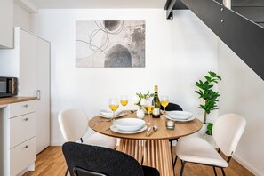 Ein Essbereich mit einem runden Tisch für vier Personen, weißen Stühlen, einem modernen abstrakten Gemälde an der Wand und einer Topfpflanze auf der rechten Seite.