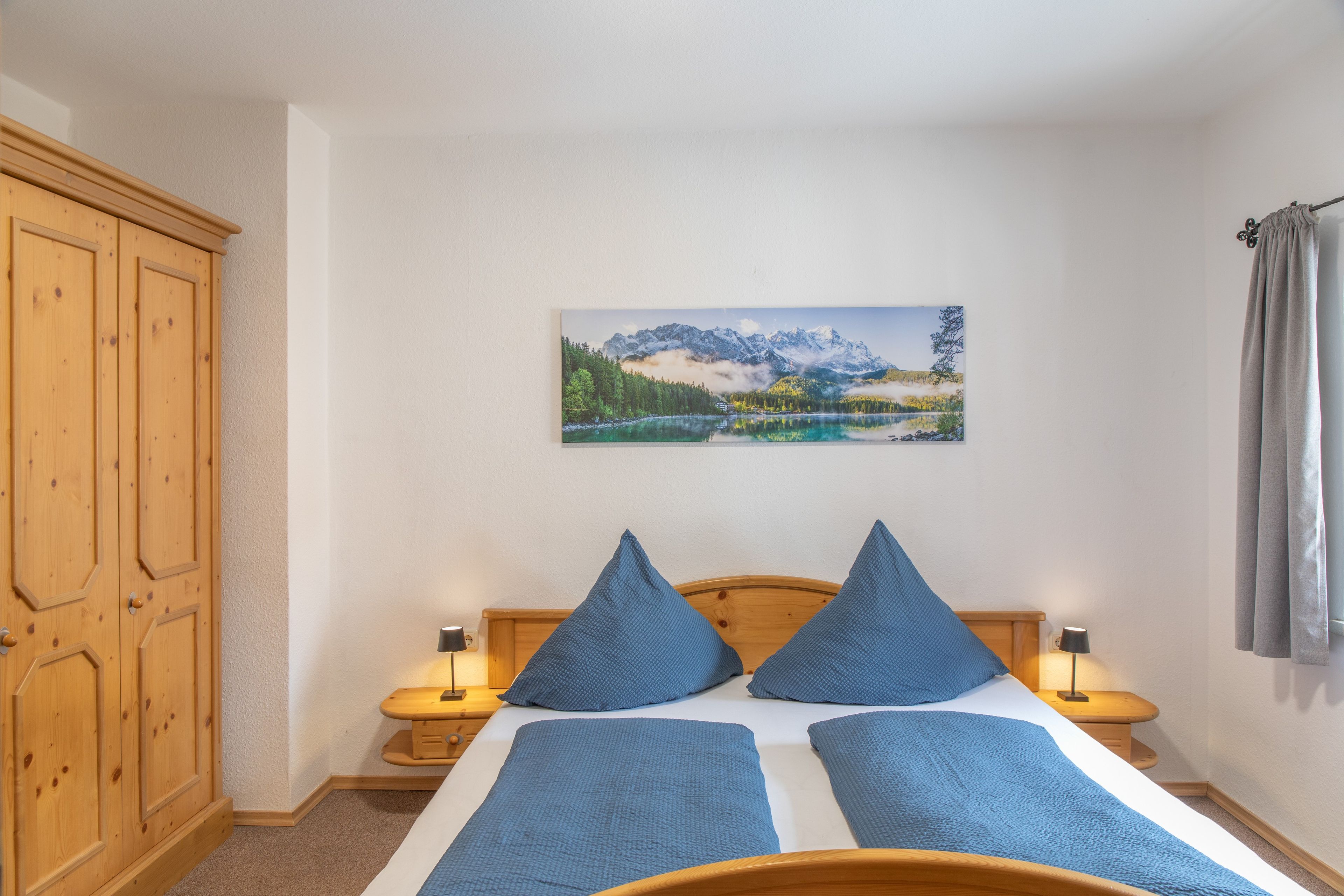 Ein Schlafzimmer mit einem Bett, zwei Kissen, einem Nachttisch mit Lampe, einem Holzschrank und einem Bild an der Wand.