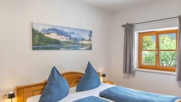 Ein Schlafzimmer mit einem Bett, Kissen, einem Nachttisch, einer Lampe, einem Fenster mit Vorhängen und einem Gemälde an der Wand.