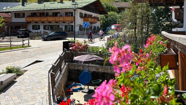 Vista de la montaña con un edificio en primer plano, una zona pavimentada con una bicicleta y un letrero que indica un restaurante.