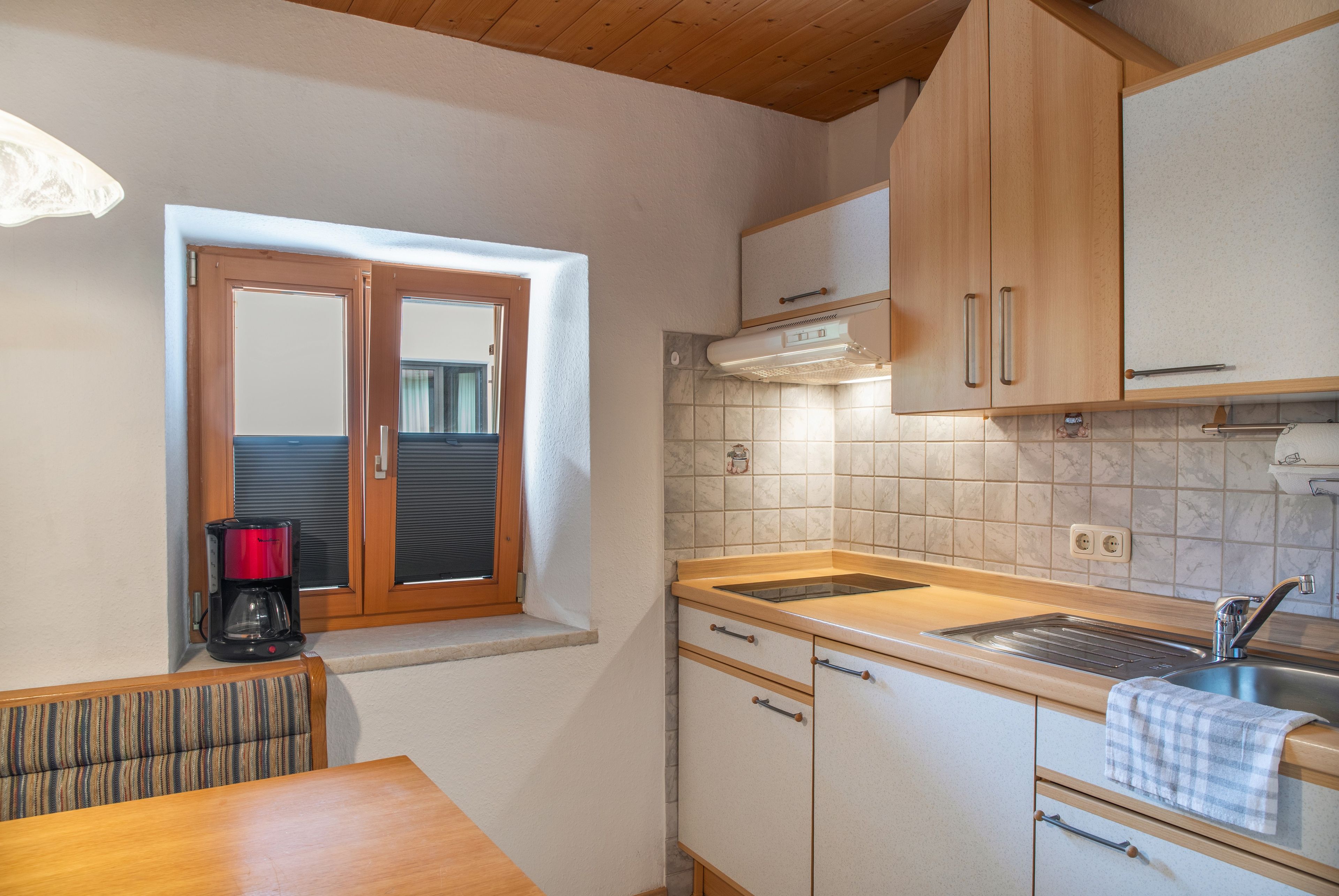 Cocina compacta con armarios de madera, horno integrado y ventana con persianas.