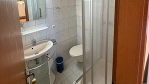 Un baño con techo de madera, un lavamanos blanco, un inodoro y una cabina de ducha de vidrio.