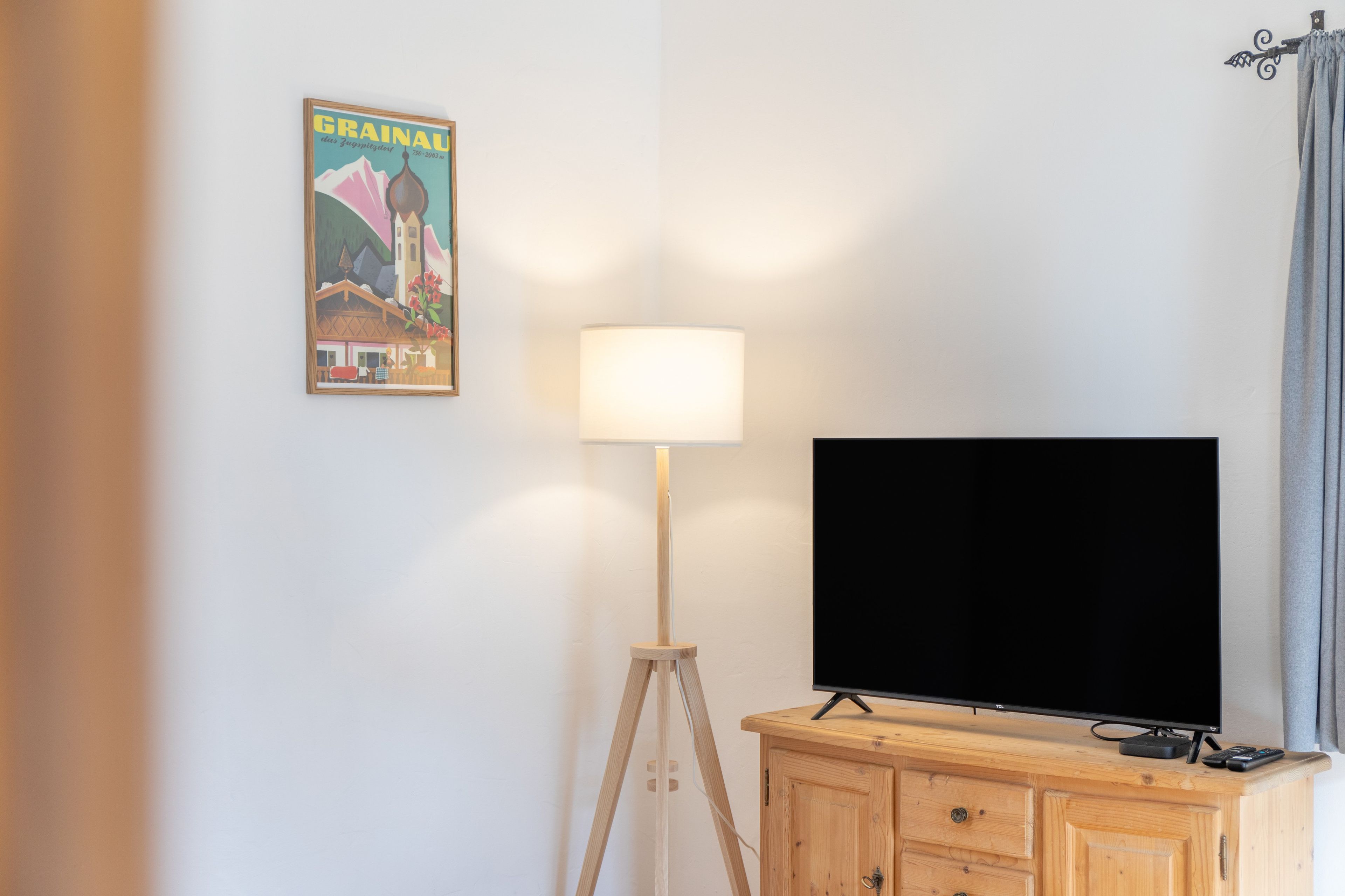 Una habitación con una televisión sobre un mueble de madera, una lámpara de pie y un cartel en la pared.