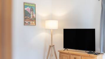 Una habitación con una televisión sobre un mueble de madera, una lámpara de pie y un cartel en la pared.
