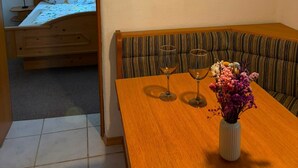 Una habitación con una mesa de comedor de madera, dos copas de vino, un jarrón con flores, un banco y un cuadro en la pared.