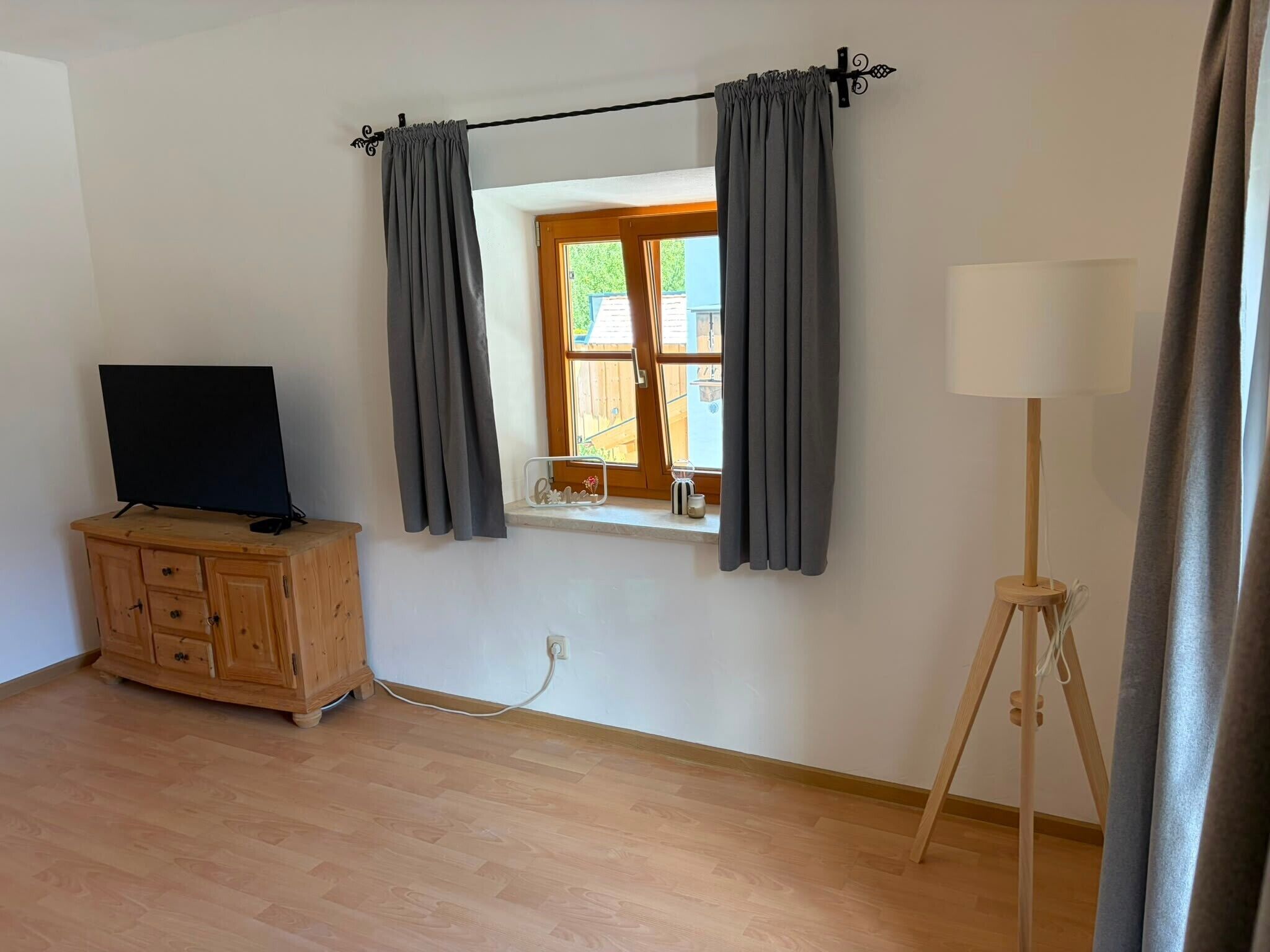 Una habitación con un armario de madera, televisor, ventana con cortinas y una lámpara de pie.