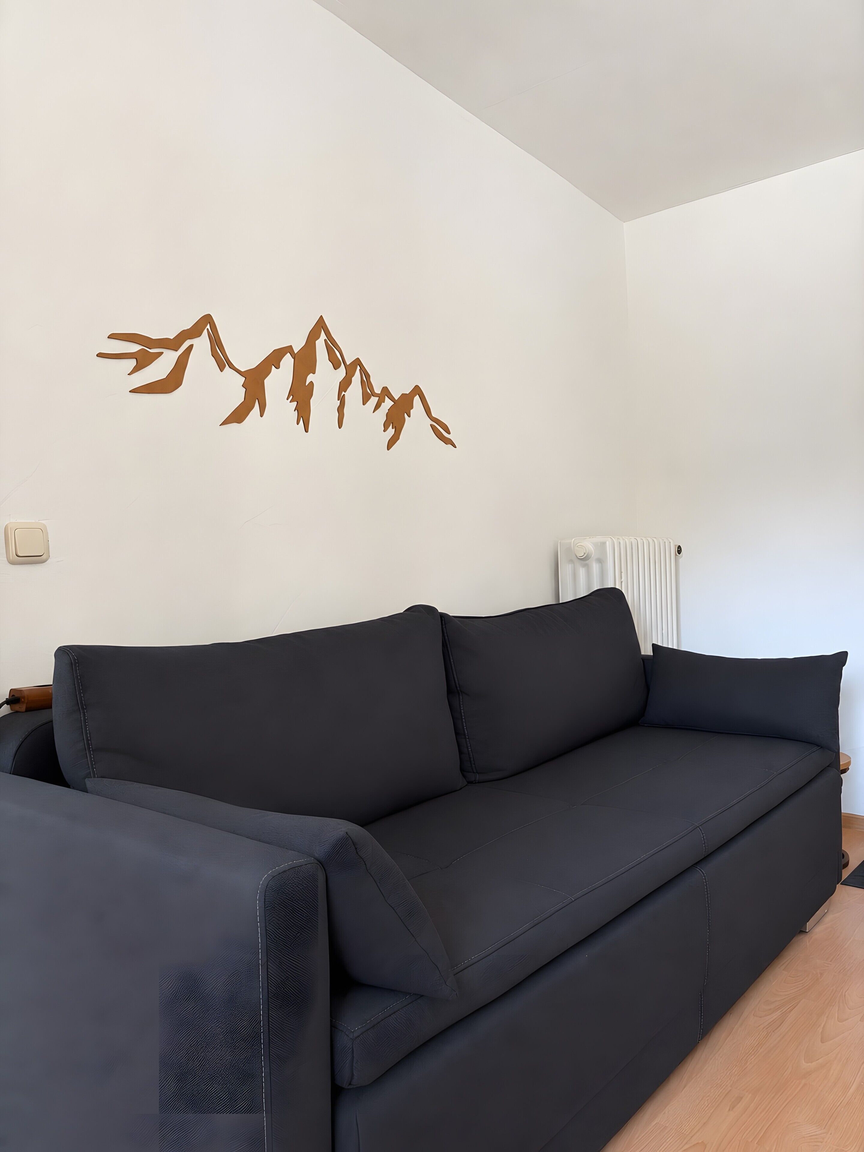 Una sala de estar moderna con un sofá negro, un radiador fijado a la pared y un adhesivo con diseño de montaña.