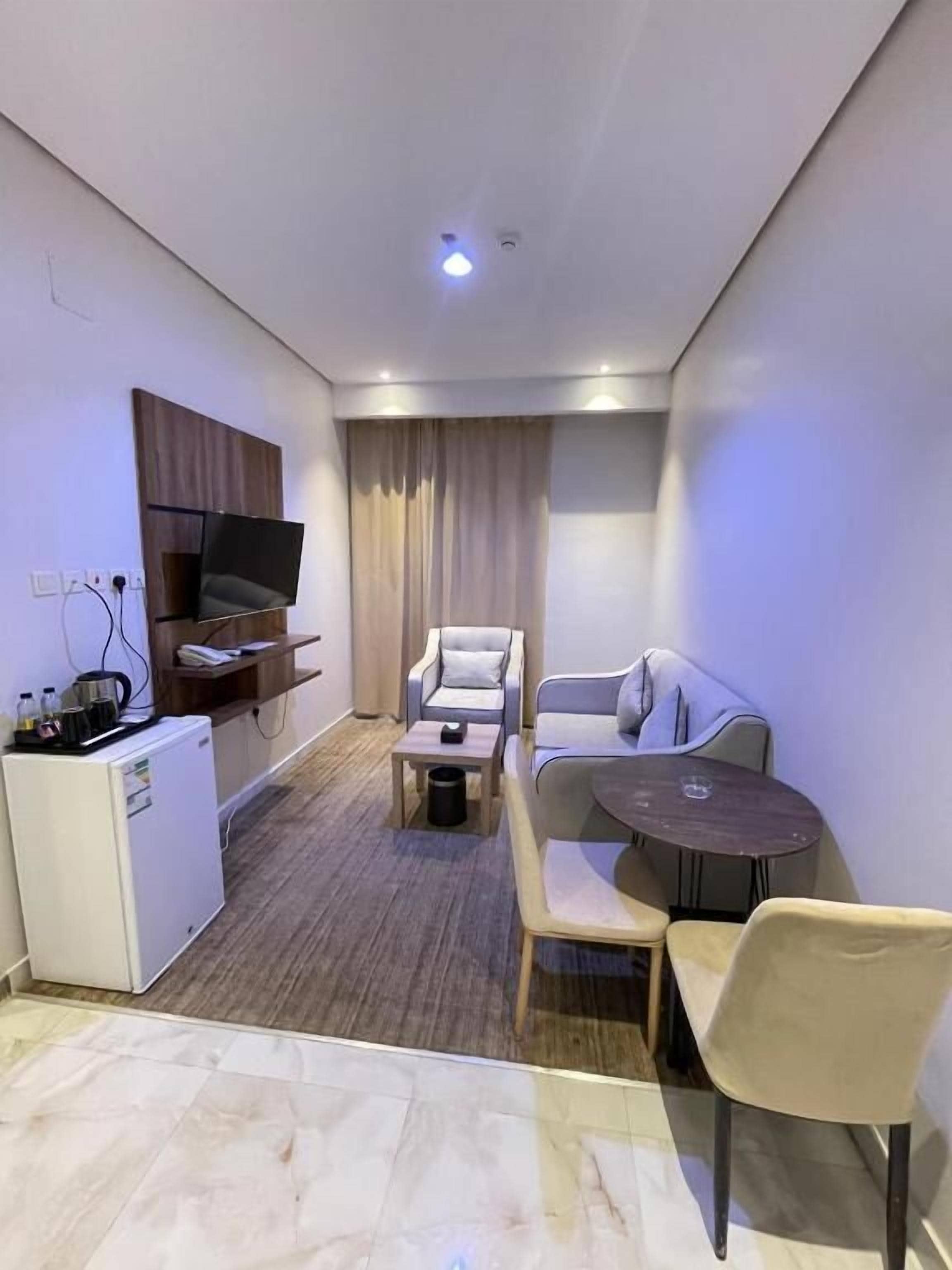 Et kompakt hotelværelse med et fladskærms TV, en sofa, et lille spisebord og et kompakt tekøkken.