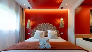 Une chambre d’hôtel moderne avec un mur d’accent rouge, une tête de lit décorative et un lit soigneusement fait, agrémenté de serviettes roulées.