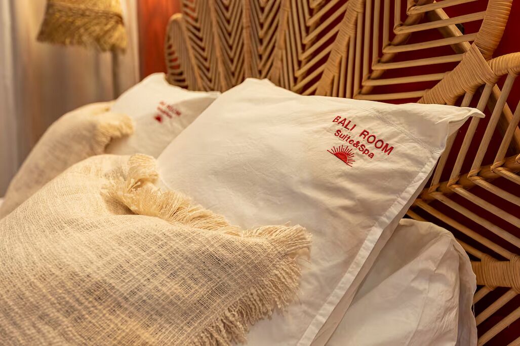 Cama con almohadas blancas y una etiqueta que indica 'BALL ROOM' con servicios de 'Sunrise & Spa'.