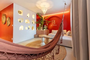 Ein Zimmer mit roter Akzentwand, einer Hängematte, einer Buddha-Statue und einem Sofa mit Kissen.