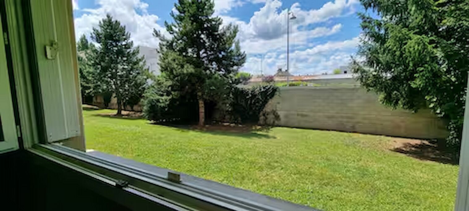 A view from a window with a grassy yard, trees, and a stone wall.