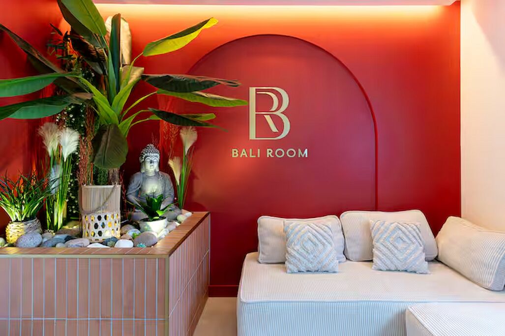 Una habitación con pared roja, sofá blanco y cojines estampados, y una estatua de Buda.