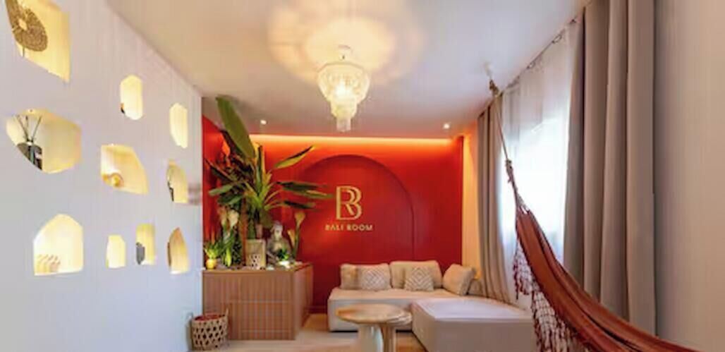 Habitación de hotel con pared de acento roja, una araña, un sofá, una mesita y una planta.