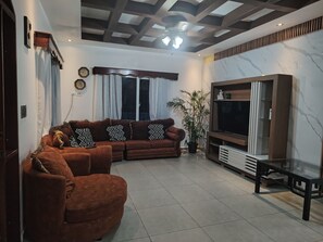 A living room with a sectional sofa, a flat-screen TV, a glass coffee table, and a potted plant. - Connection, fun, relaxation—Villas Flores: a spacious home to enjoy. (TELA)