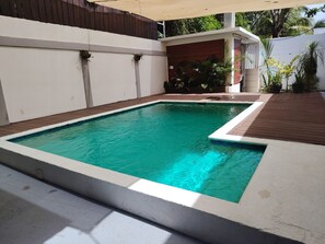 A rectangular swimming pool with a white border, surrounded by a wooden deck and a white wall. - Connection, fun, relaxation—Villas Flores: a spacious home to enjoy. (TELA)