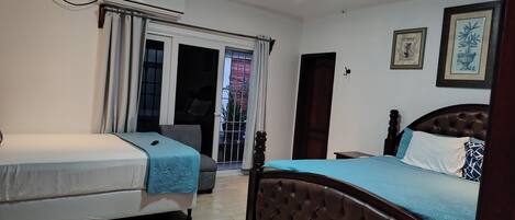 Un dormitorio con dos camas, una ventana con cortinas, un ventilador de techo y una puerta que da a un balcón.