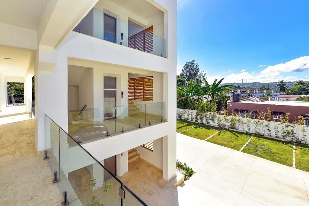 A modern two-story building with a glass balcony and a view of a landscaped garden.