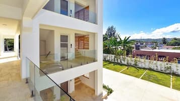A modern two-story building with a glass balcony and a view of a landscaped garden.