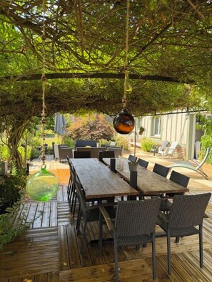 An outdoor patio with a wooden table and chairs, surrounded by greenery and a pergola structure. - Large, charming vacation rental for 15 people (Barentin)