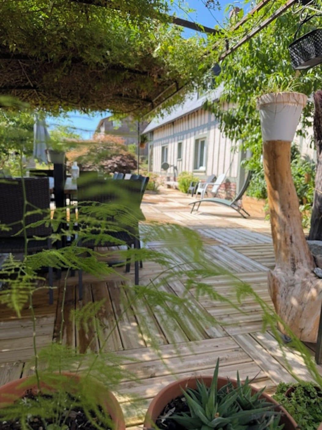Une terrasse extérieure avec un sol en bois, des plantes en pot et une vue sur un bâtiment en arrière-plan.