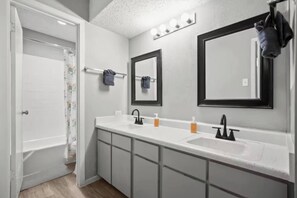 A bathroom with a double sink, two mirrors, a towel rack, and a shower curtain. - Bright Stay • DT Austin • Pecan St. Festival Ready (Austin)