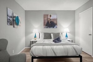 A modern bedroom with a large bed, two bedside tables with lamps, a chair, and artwork on the walls. - Bright Stay • DT Austin • Pecan St. Festival Ready (Austin)