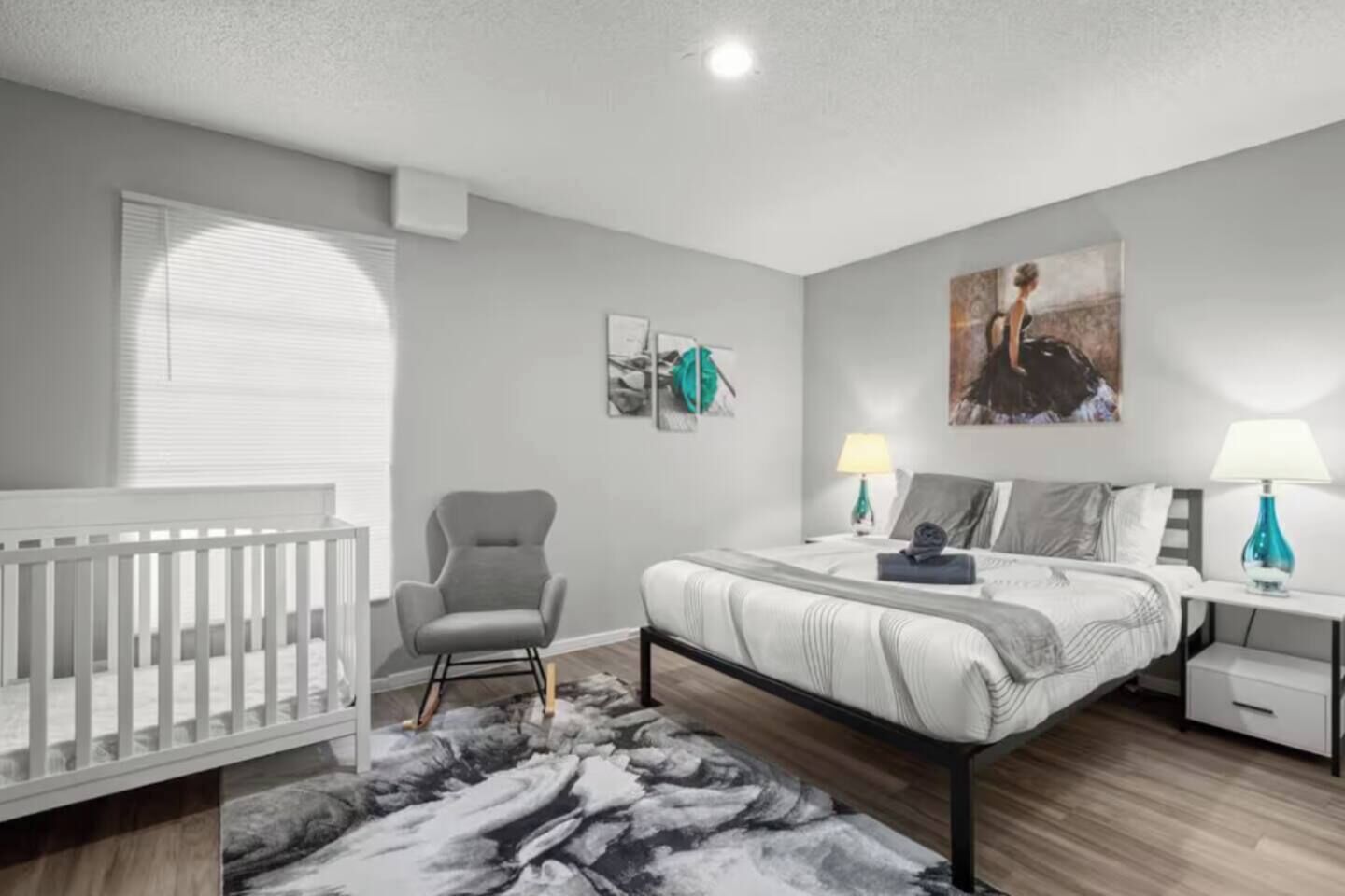 A bedroom with a crib, a bed, a chair, and artwork on the walls.