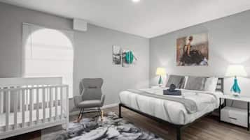 A bedroom with a crib, a bed, a chair, and artwork on the walls.