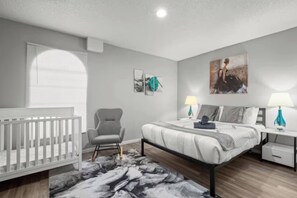 Ein Schlafzimmer mit einem Kinderbett, einem Bett, einem Sessel und Bildern an den Wänden.