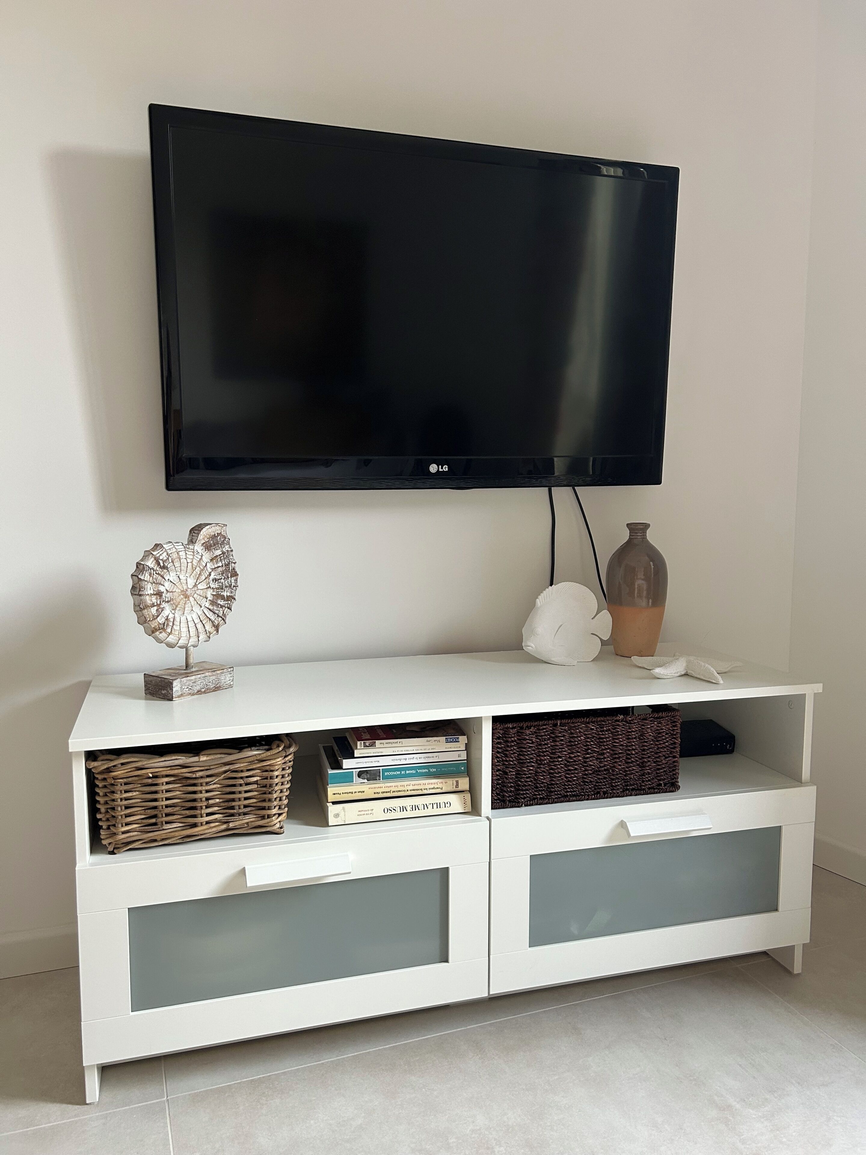 Un meuble de rangement blanc pour appareils électroniques, avec un téléviseur à écran plat fixé au-dessus.