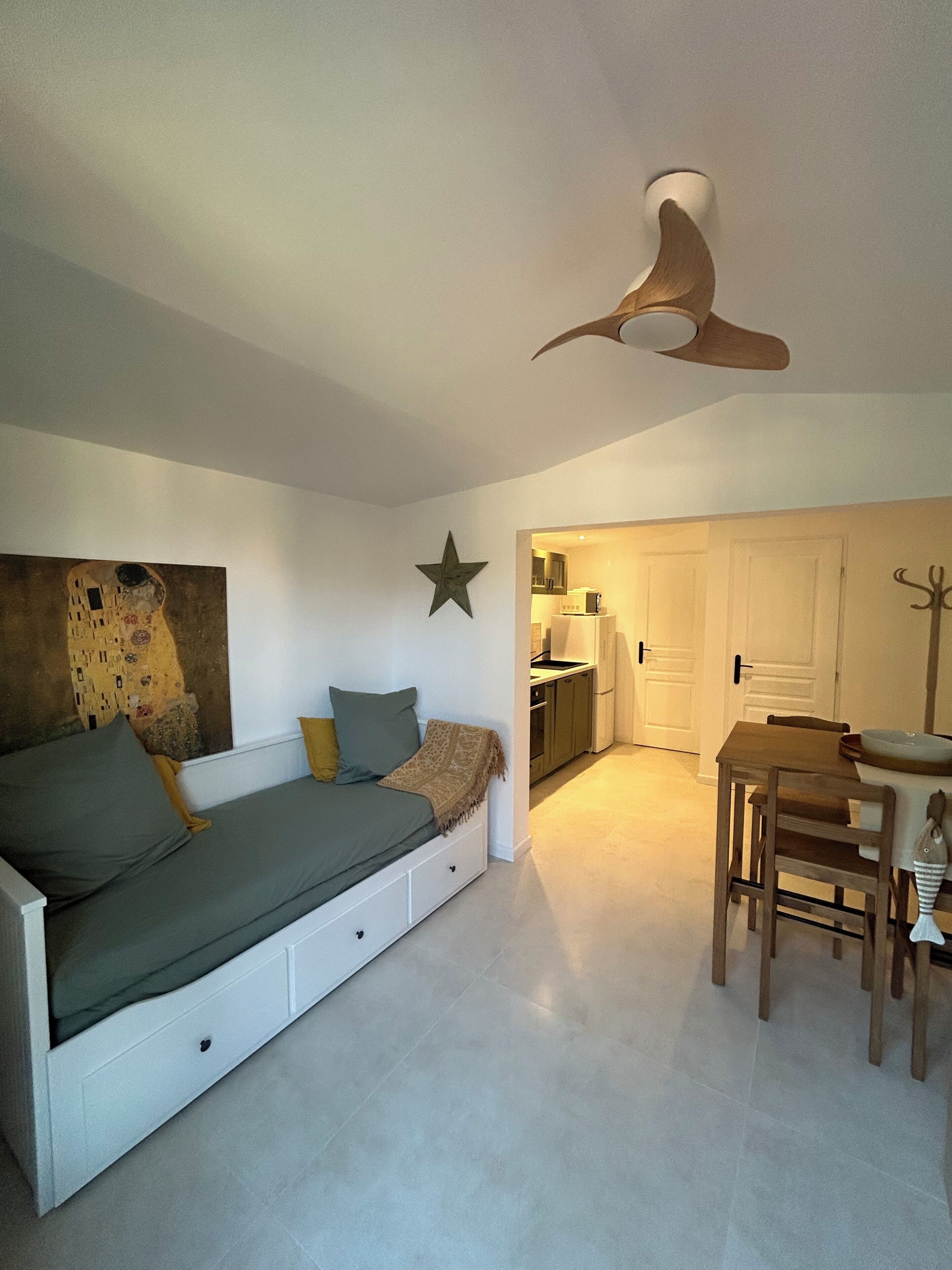 A modern bedroom with a built-in sofa bed, a star decoration, a ceiling fan, and a view into the kitchen.
