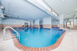 An indoor swimming pool with clear blue water, surrounded by a tiled floor and walls, with visible poolside railings and a ceiling with exposed pipes and lighting fixtures. - Phoenix V 104 2 Bedroom Condo (Orange Beach)