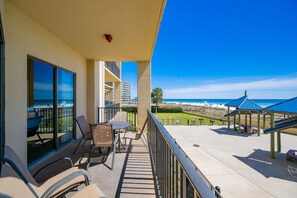 Ein Balkon mit Tisch und Stühlen, mit Blick auf einen Strand und einen Parkplatz.